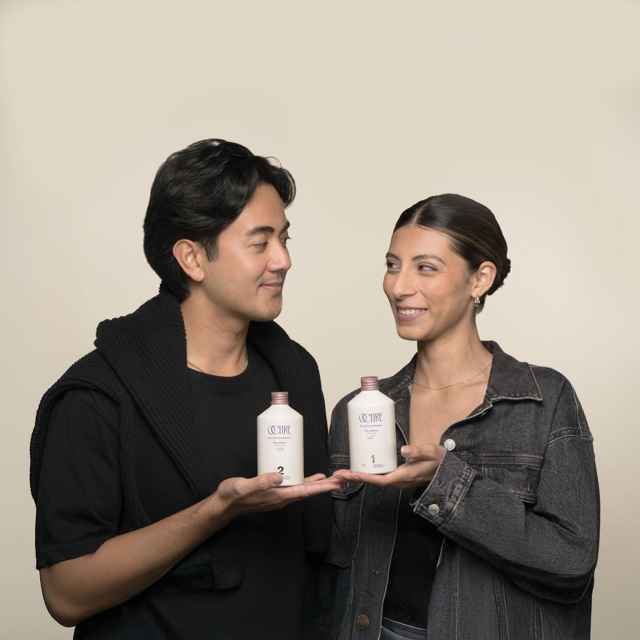 Smiling male and female models holding OCHRE Purifying Shampoo and Essential Conditioner