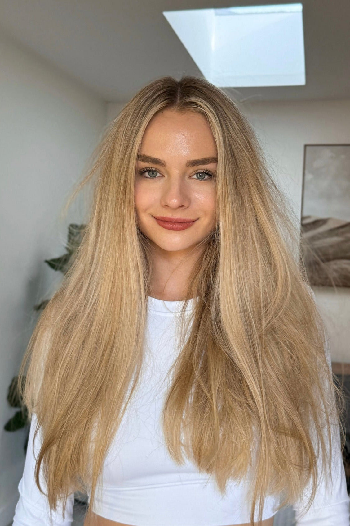 Woman with long blonde hair wearing a white top indoors.