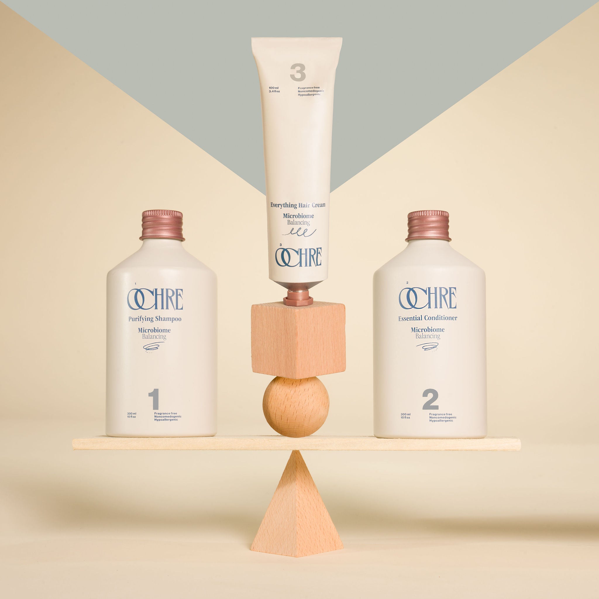 OCHRE Purifying Shampoo, Essential Conditioner, and Everything Hair Cream balancing on wooden board on stylized background
